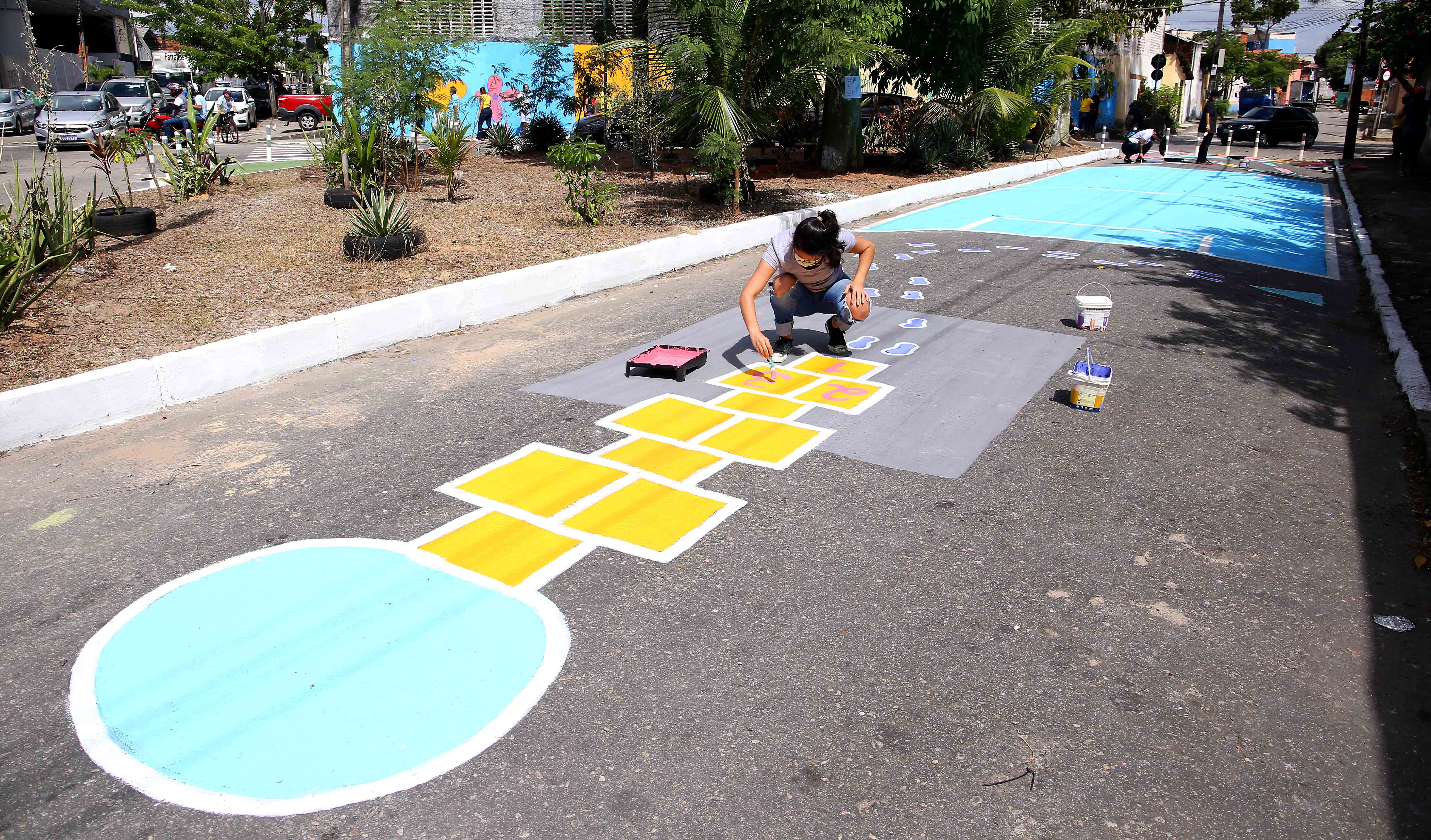 uma mulher pinta um jogo de amarelinha numa rua